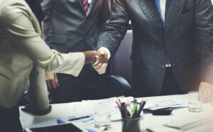 Two people shaking hands over a desk with papers on